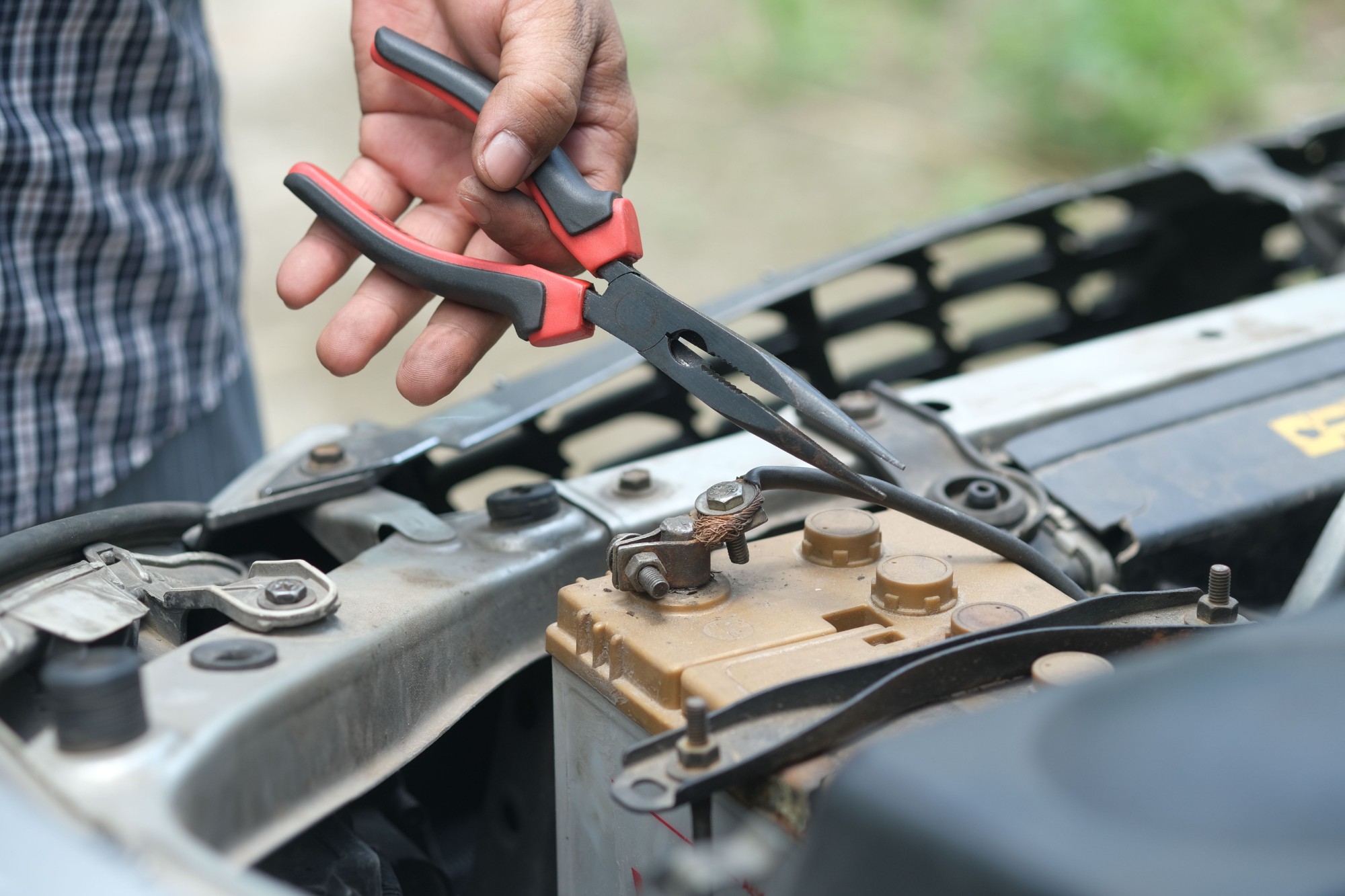 Hand holding long-nose pliers beside a car battery terminal